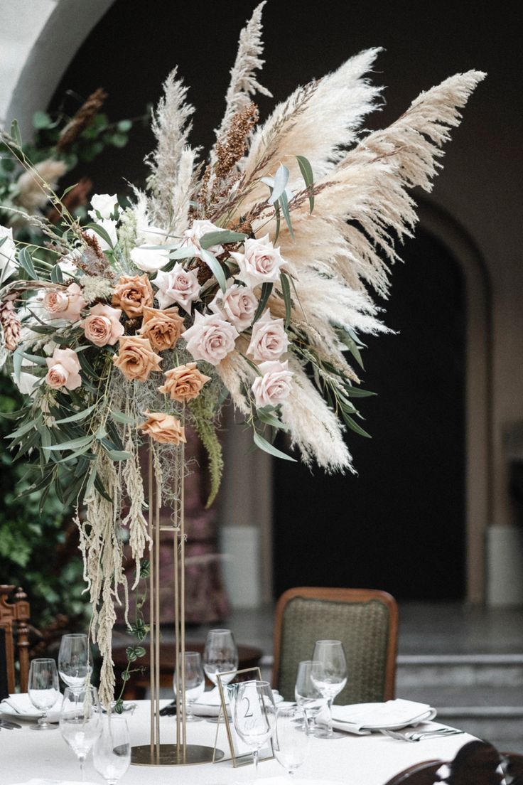 a tall vase filled with lots of flowers on top of a white table cloth covered table