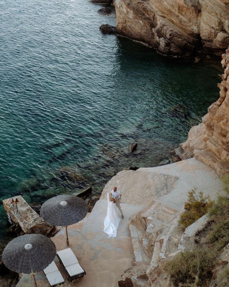 a bride and groom standing on the edge of a cliff by the ocean with umbrellas