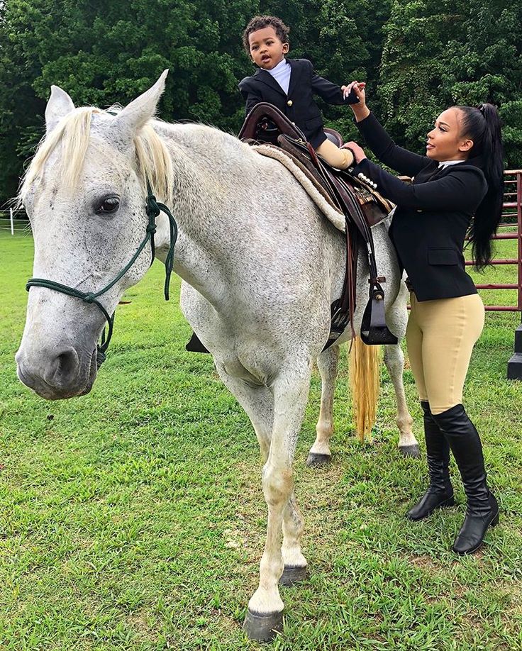 a woman holding the reigns of a white horse with a young boy on it's back