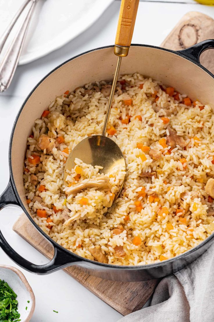 a pot filled with rice and vegetables on top of a wooden cutting board next to utensils