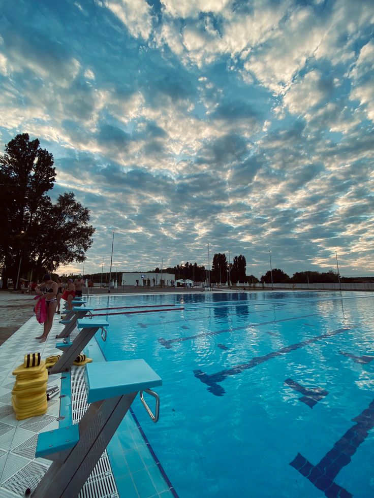 people are standing at the edge of an empty swimming pool as the sun goes down