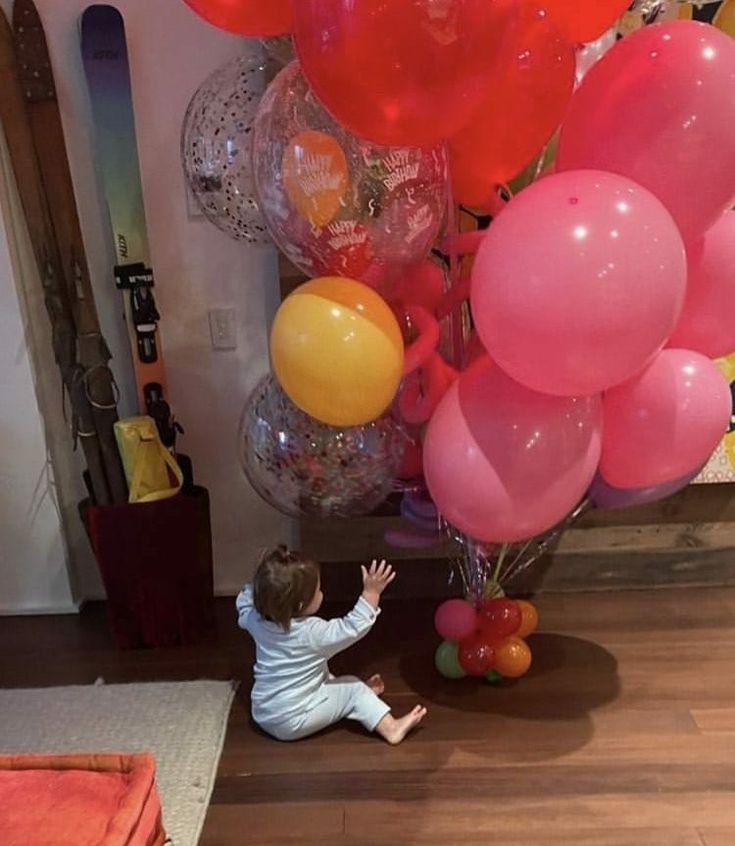 a small child reaching up at some balloons on the floor in front of a wall