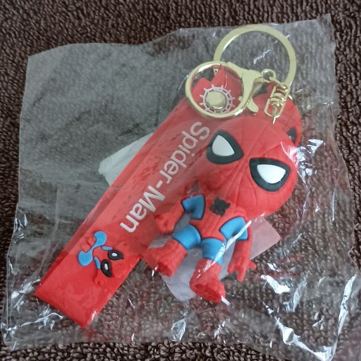 a red keychain with a spiderman figure on it sitting on top of a plastic bag