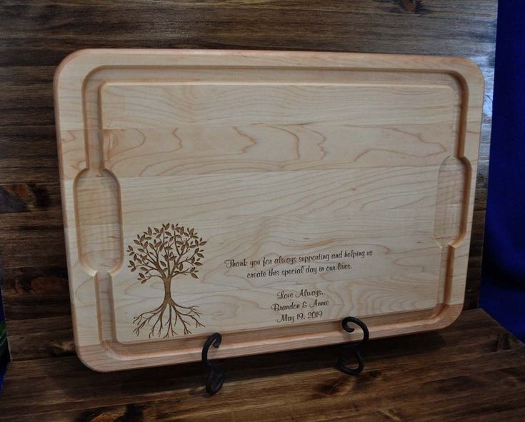 a wooden cutting board with a tree on it and two hooks holding the cutting board