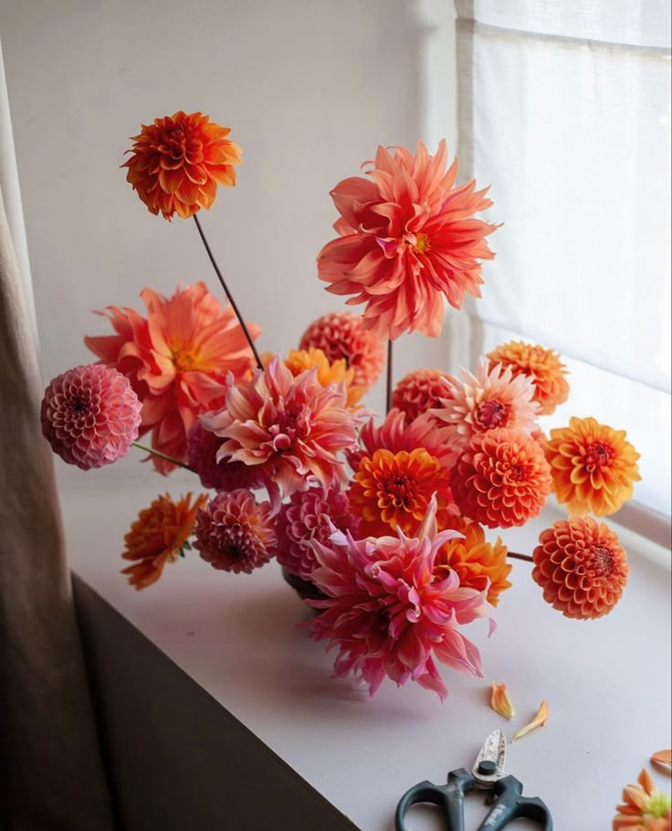 an arrangement of flowers in a vase on a window sill next to some scissors