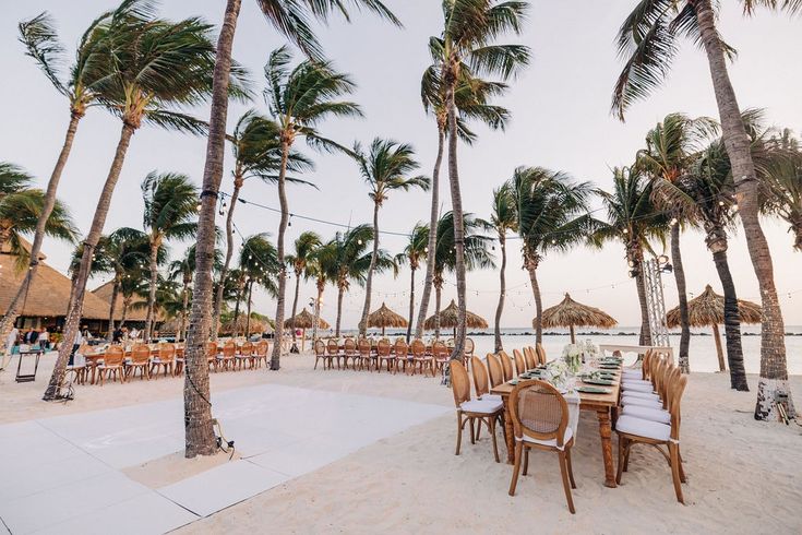 a table set up on the beach with palm trees