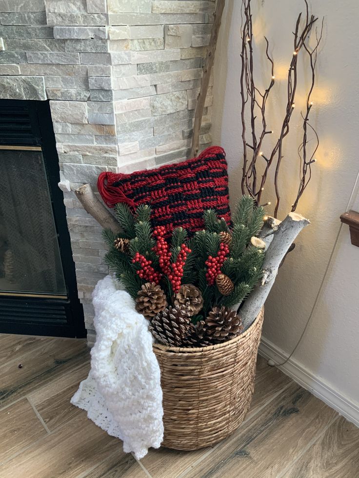 a basket filled with pine cones and red berries next to a fire place in front of a fireplace