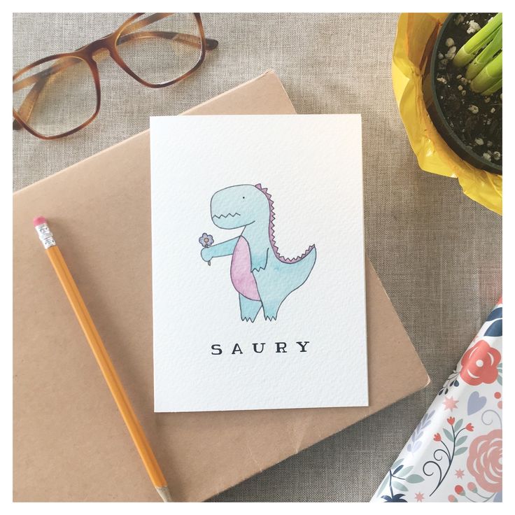 a card with a dinosaur on it next to some pencils and eyeglasses