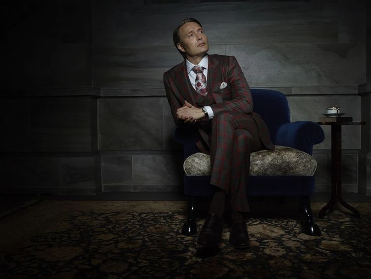 a man in a suit and tie sitting on a blue chair with his hands crossed