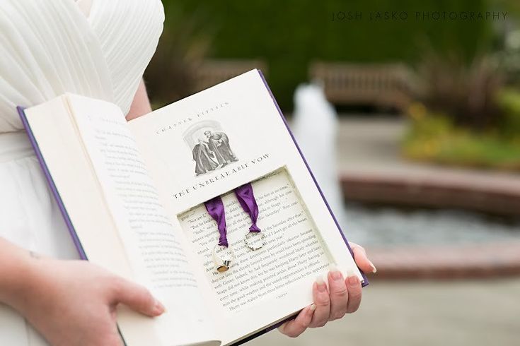 a woman in a white dress holding an open book with a purple ribbon around it