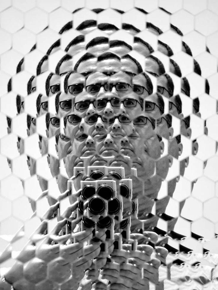 a man holding a camera taking a selfie in front of some hexagonal shapes