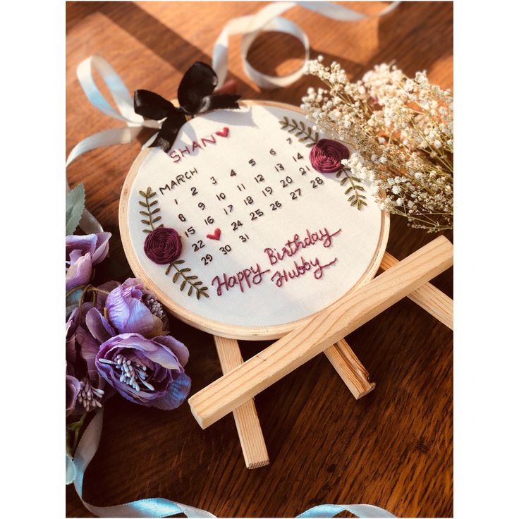 a cross - stitch birthday card with flowers and ribbons on the table next to it