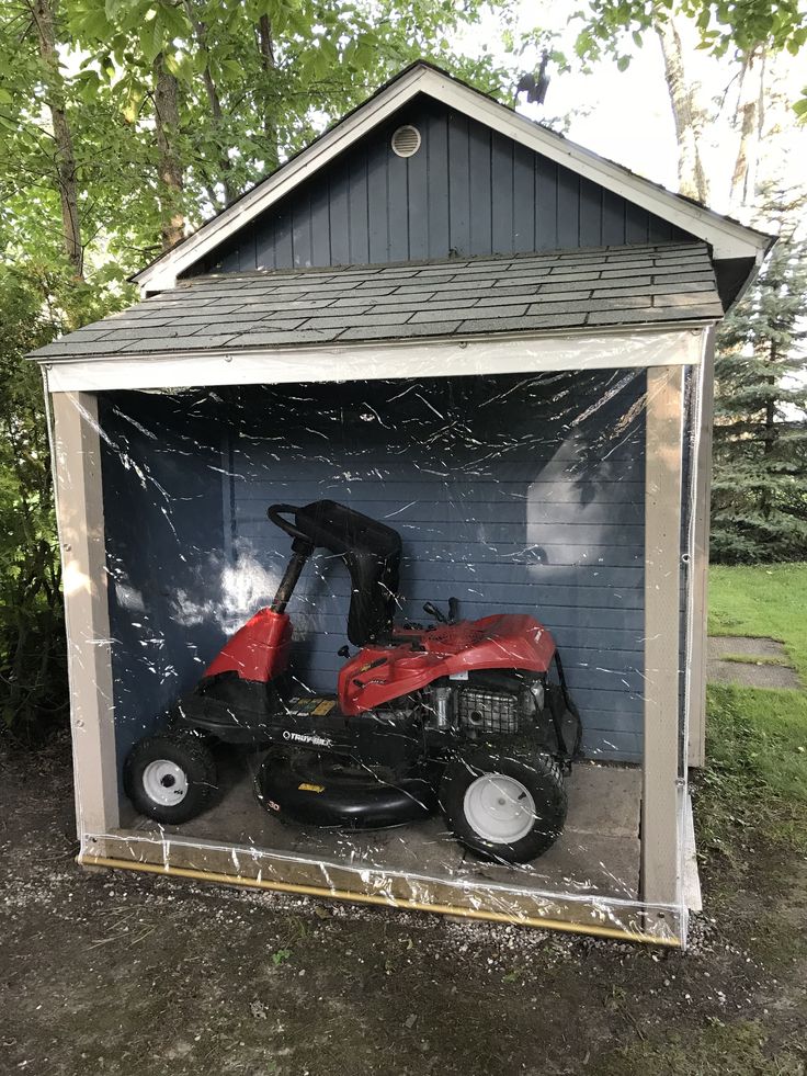 a red lawn mower sitting inside of a small shed on the side of a road