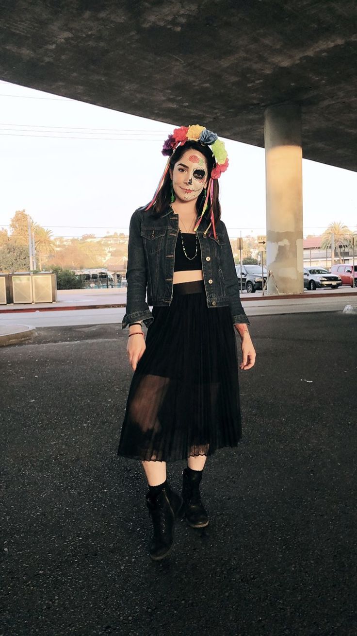 a woman in a black dress and jean jacket with flowers on her head standing under an overpass