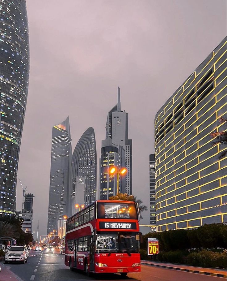 a red double decker bus driving down a street next to tall buildings in the city