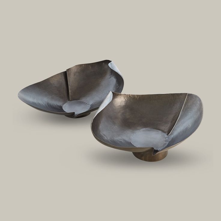 two metal bowls sitting next to each other on top of a gray surface with one bowl in the middle