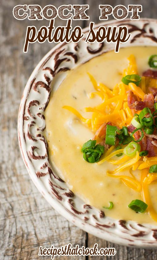 a bowl of potato soup with cheese and green garnish on top, sitting on a wooden table