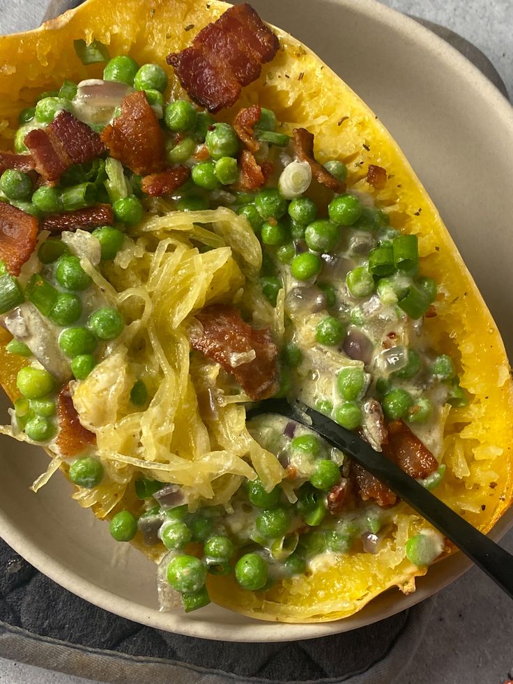 a white bowl filled with pasta and peas on top of a gray table cloth next to a fork