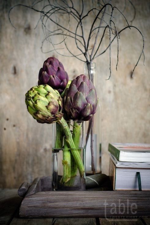 three artichokes in a glass vase on a table next to two books