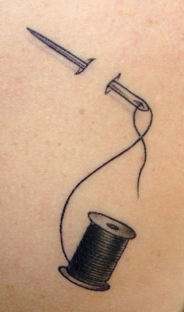 a drawing of a thread spool and needle on the back of a woman's shoulder