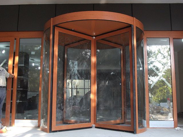 a man standing in front of an open wooden revolving door with glass doors on both sides