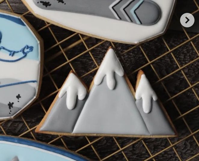 cookies decorated with frosting and mountains are sitting on a wire rack next to plates