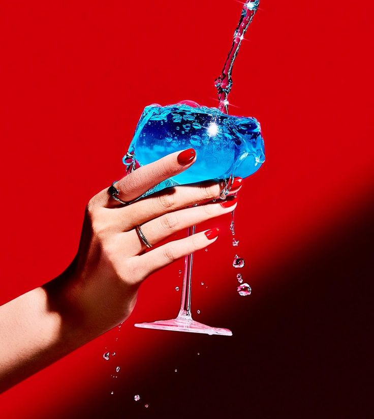 a woman's hand holding a blue drink in front of a red background with water splashing on it