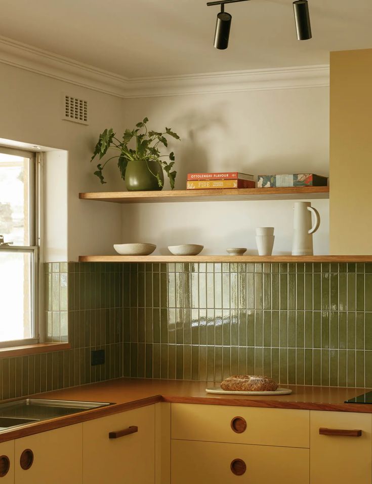 a kitchen with yellow cabinets and green tile backsplash, potted plant on the shelf