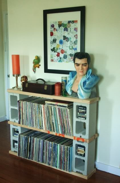 a man is sitting on top of a book shelf with records and cds in front of him