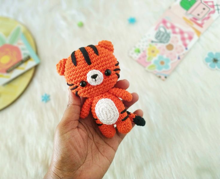 a hand holding a small crocheted stuffed animal in the shape of a tiger