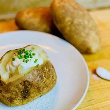 a baked potato with sour cream and chives on a white plate next to two potatoes