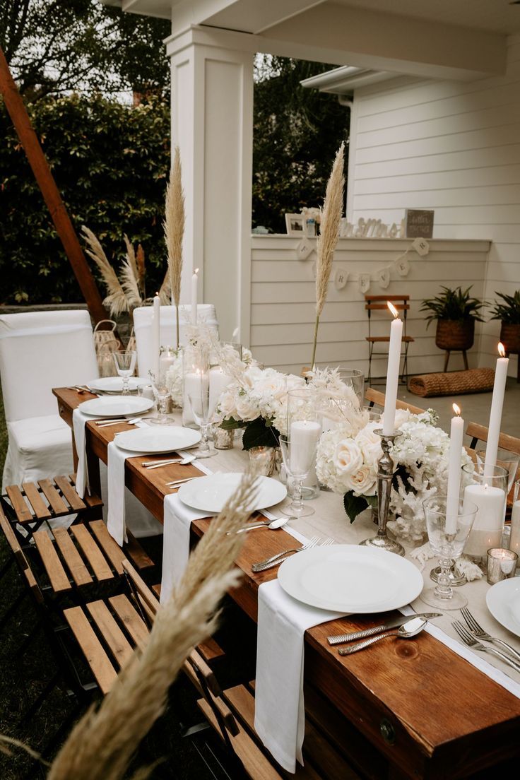 a table set with white flowers and candles for an outdoor dinner party in the backyard