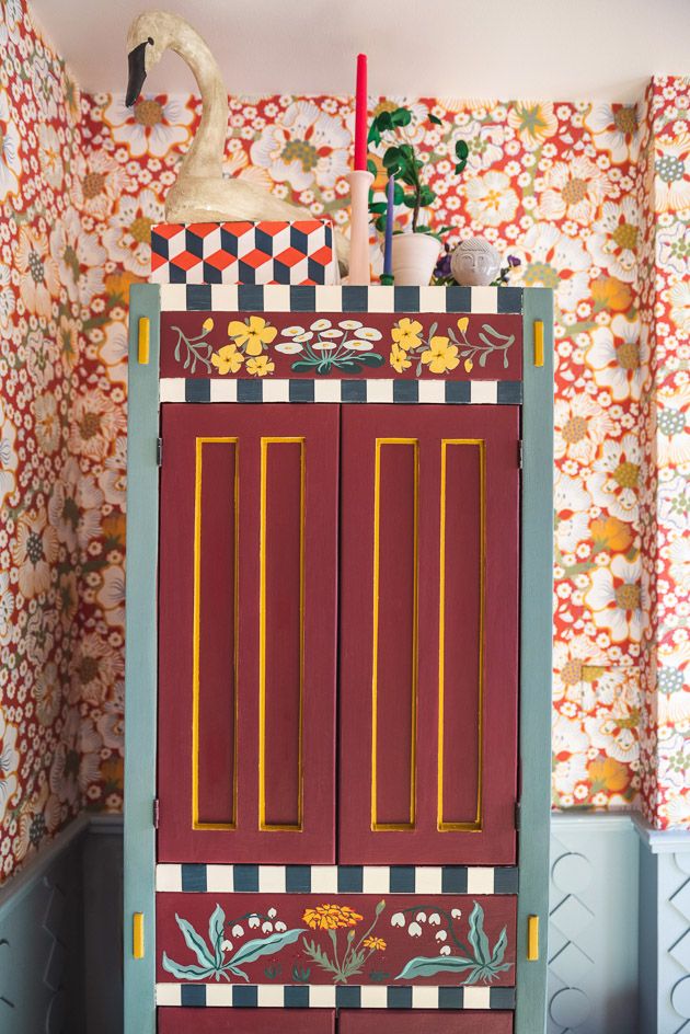 a tall cabinet painted with flowers and birds on it's sides in front of a wallpapered background