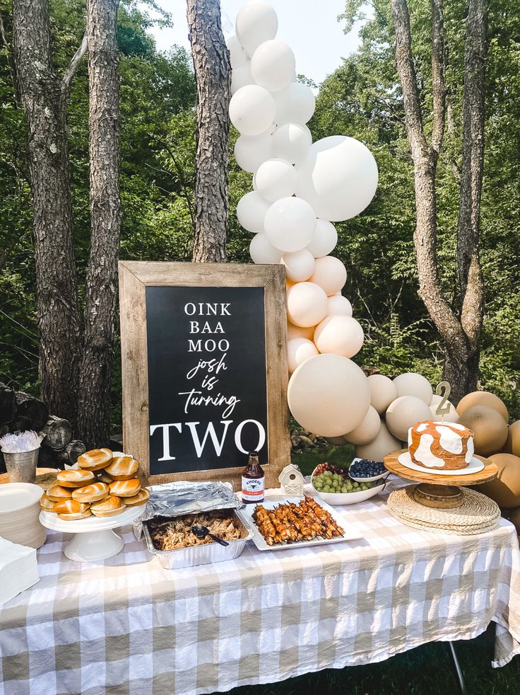 a table topped with lots of food next to a forest filled with trees and balloons