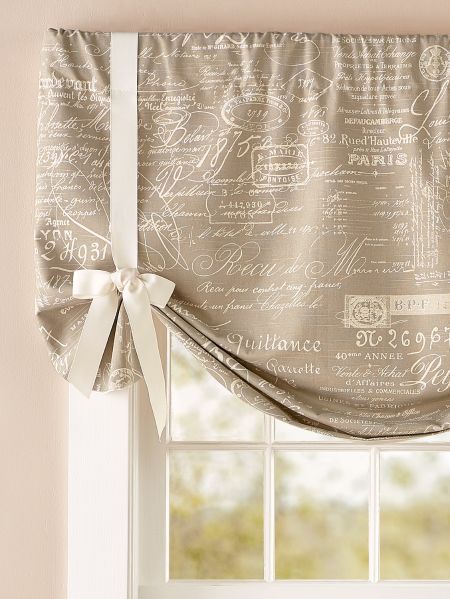 a window curtain with writing on it and a bow tie at the top, in front of a window