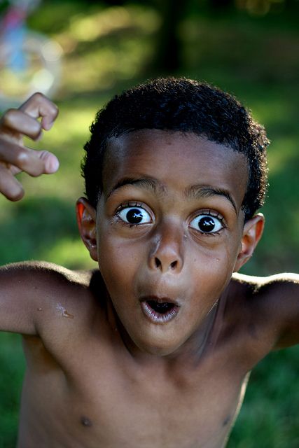 a young boy making a face with his hands and eyes wide open in the grass