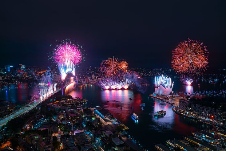 fireworks lit up the night sky over a city and river with boats on it's side