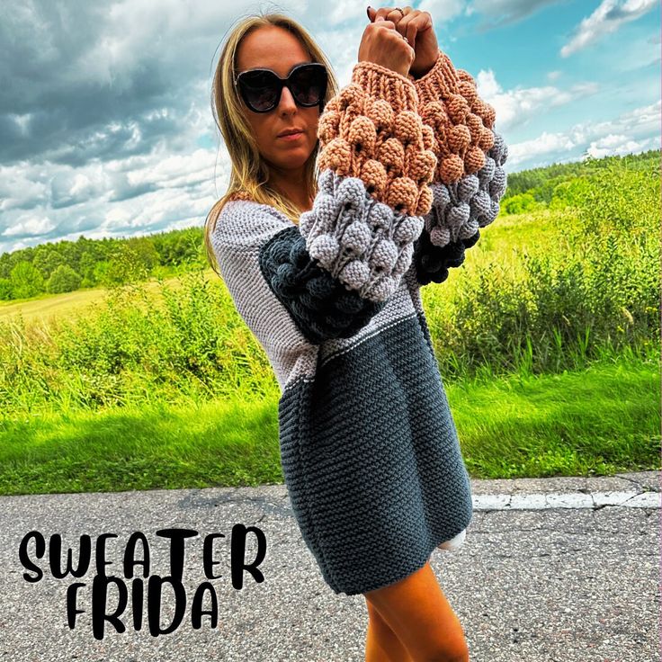 a woman is holding up a crocheted sweater in the middle of the road