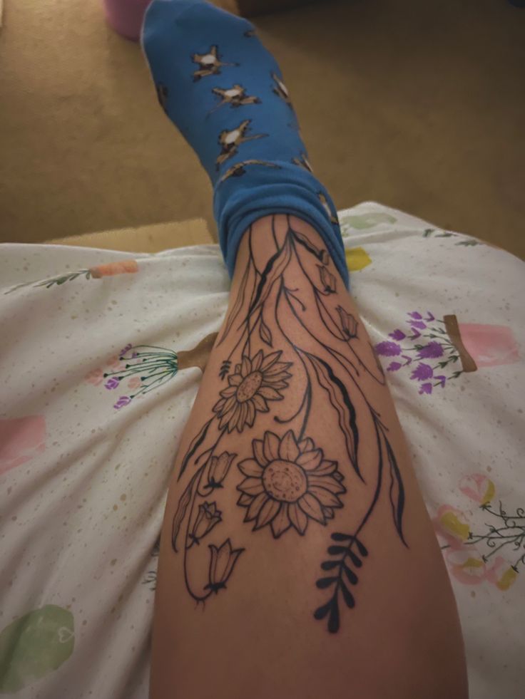 a woman's leg with flowers and leaves on it, sitting on a bed