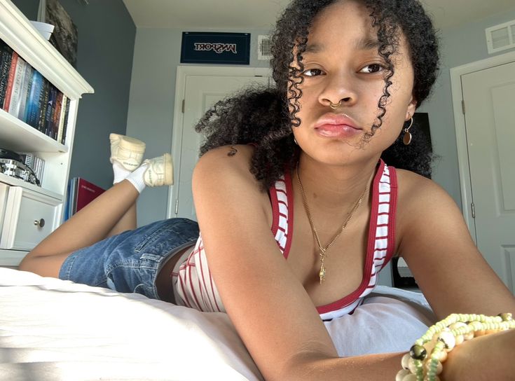 a woman with curly hair laying on top of a bed next to a book shelf