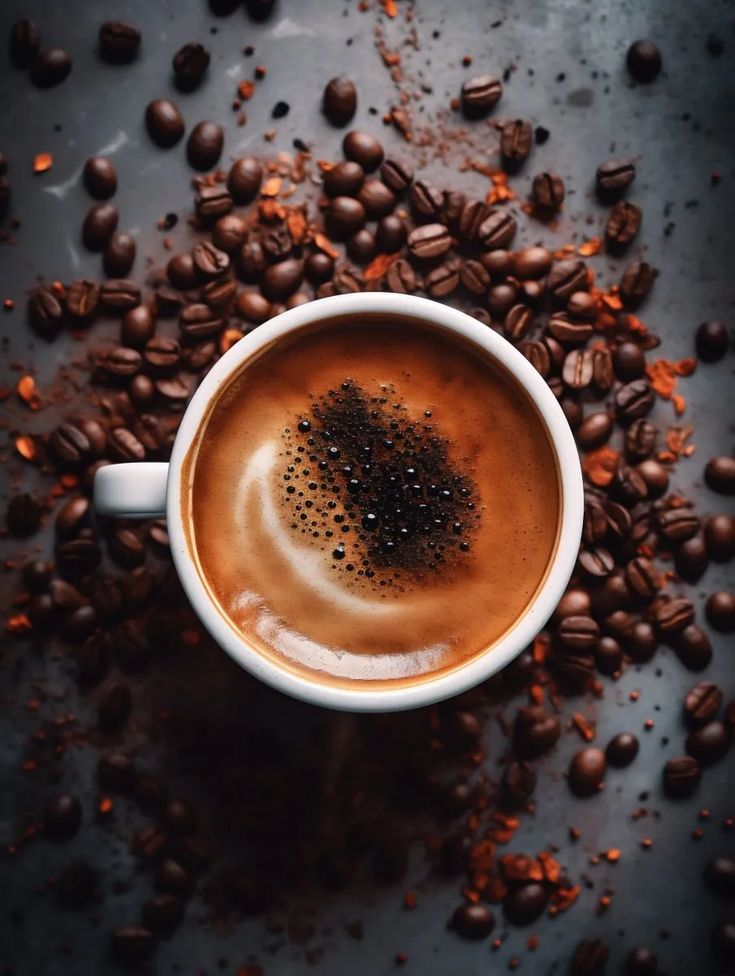 there is a cup of coffee on the table with beans and cinnamons around it