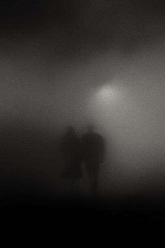 two people standing in the fog under a street light