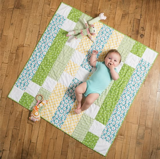 a baby laying on top of a wooden floor next to a stuffed animal and blanket