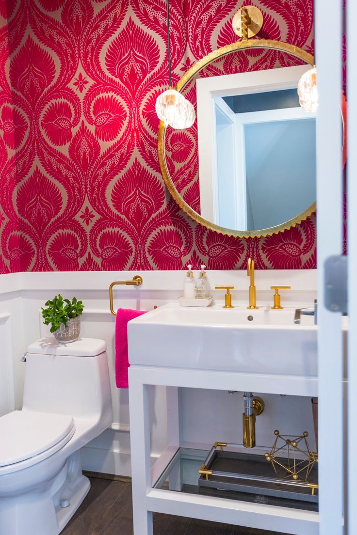 a bathroom with red and gold wallpaper, white sink, toilet and mirror in it