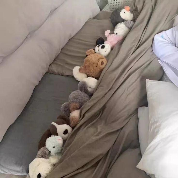 stuffed animals are lined up in the corner of a bed, with sheets pulled back