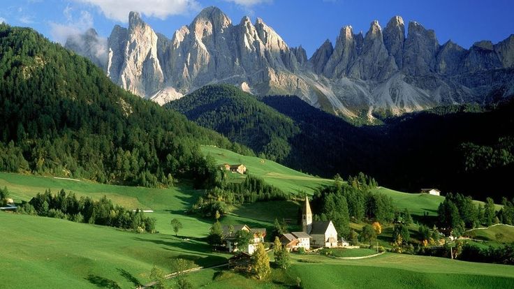 the mountains are covered with green grass and trees, while houses stand in the foreground