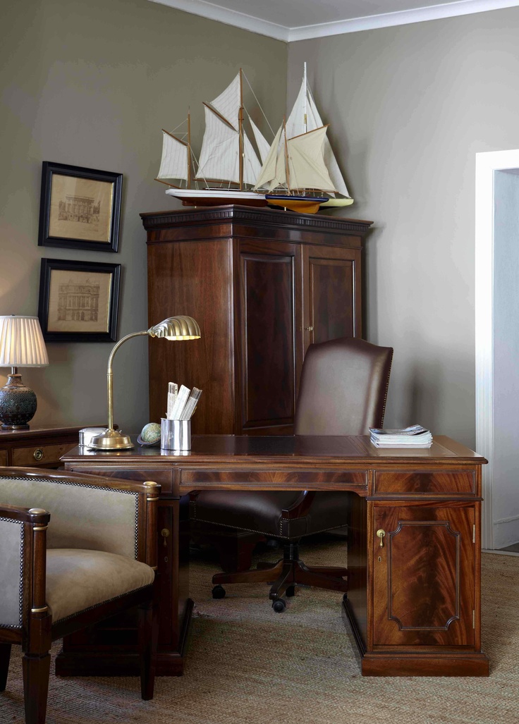 a wooden desk topped with a computer monitor and a lamp next to a cabinet filled with books