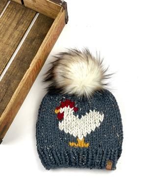 a knitted hat with a pom - pom sits next to a wooden crate