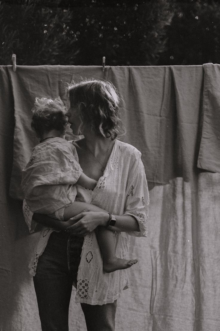 a black and white photo of a woman holding a baby in her arms while standing next to a clothes line