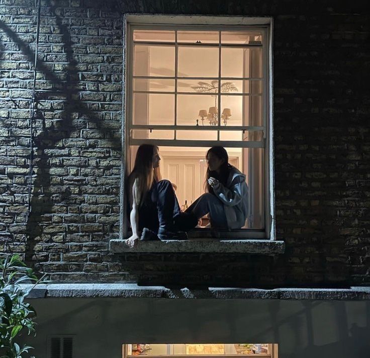 two women sitting on the ledge of a window at night